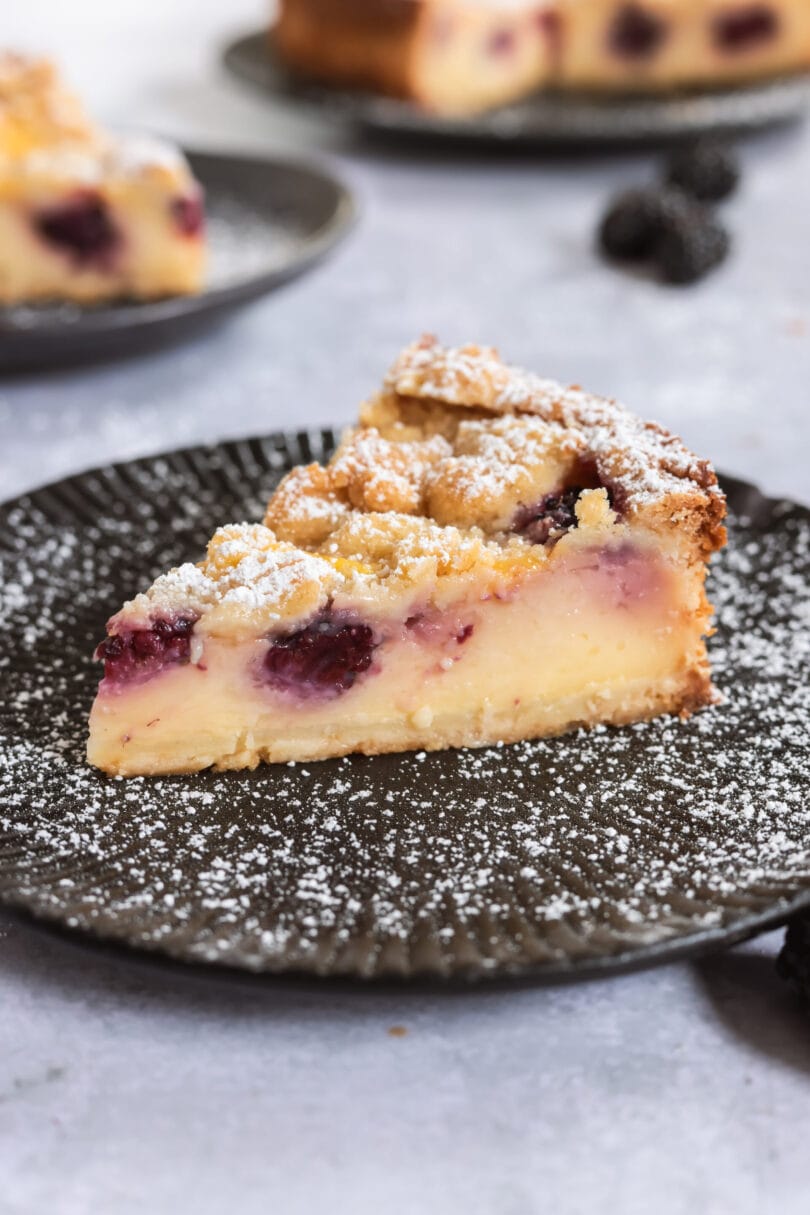 Nahaufnahme eines veganen Brombeerkuchens mit Puddingfüllung, Brombeeren und knusprigen Streuseln.