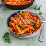 Schale mit veganen Penne alla Vodka in cremiger Tomatensauce, garniert mit Petersilie und veganem Parmesan.