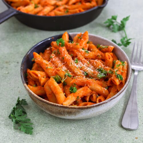 Schale mit veganen Penne alla Vodka in cremiger Tomatensauce, garniert mit Petersilie und veganem Parmesan.