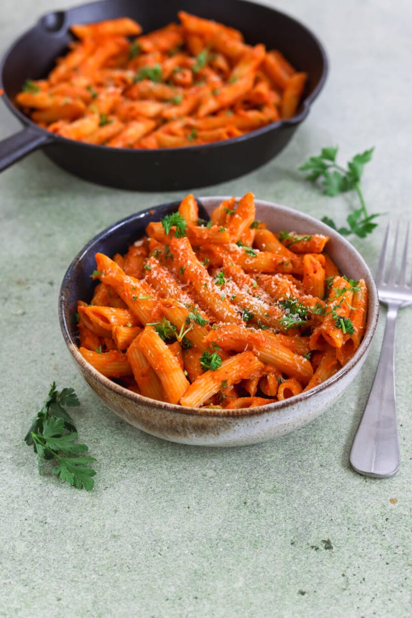 Schale mit veganen Penne alla Vodka in cremiger Tomatensauce, garniert mit Petersilie und veganem Parmesan.
