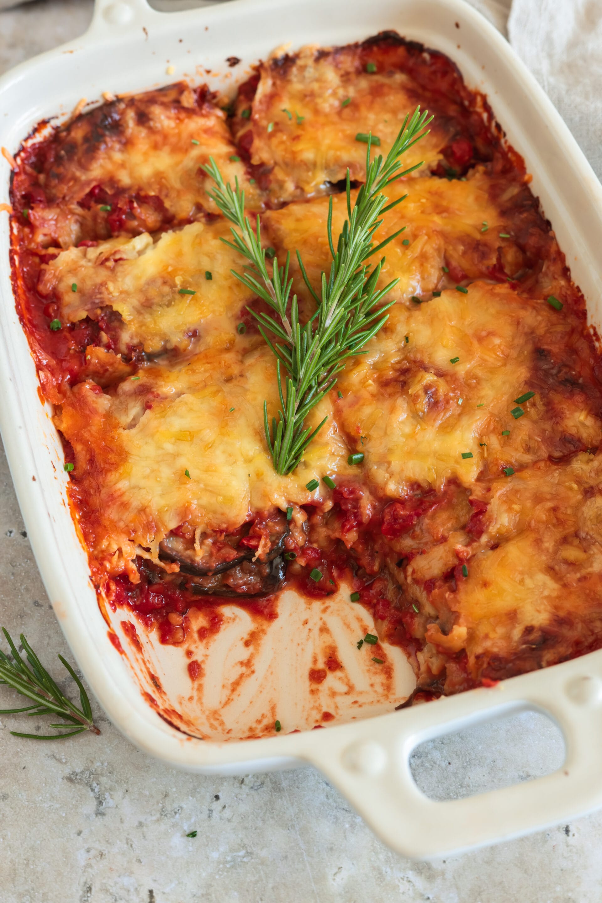 Veganer Auberginenauflauf mit Tomatensauce und knusprig überbackenem Streukäse, angeschnitten in der Auflaufform.