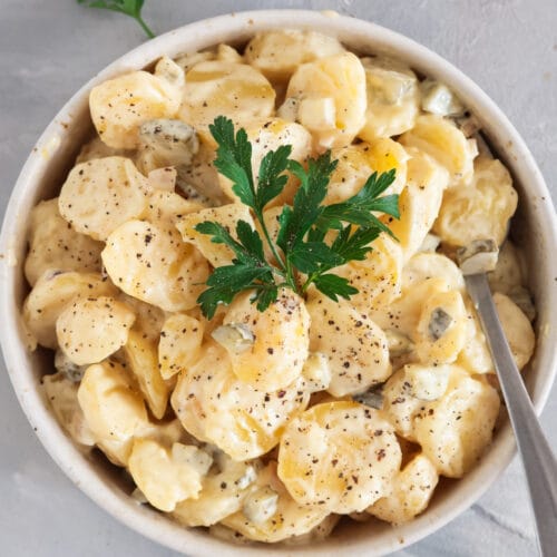 Veganer Kartoffelsalat mit Brühe und Mayo in heller Schale, garniert mit frischer Petersilie und Pfeffer