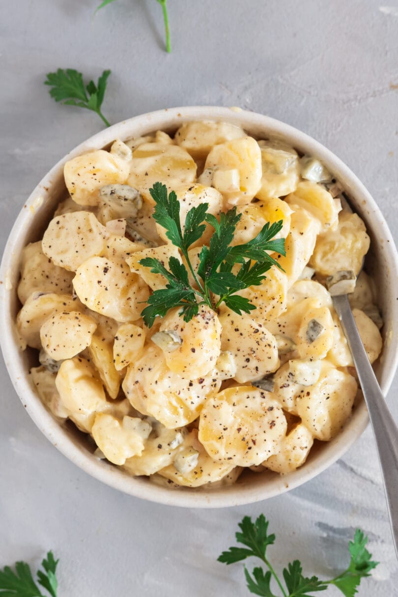 Veganer Kartoffelsalat mit Brühe und Mayo in heller Schale, garniert mit frischer Petersilie und Pfeffer