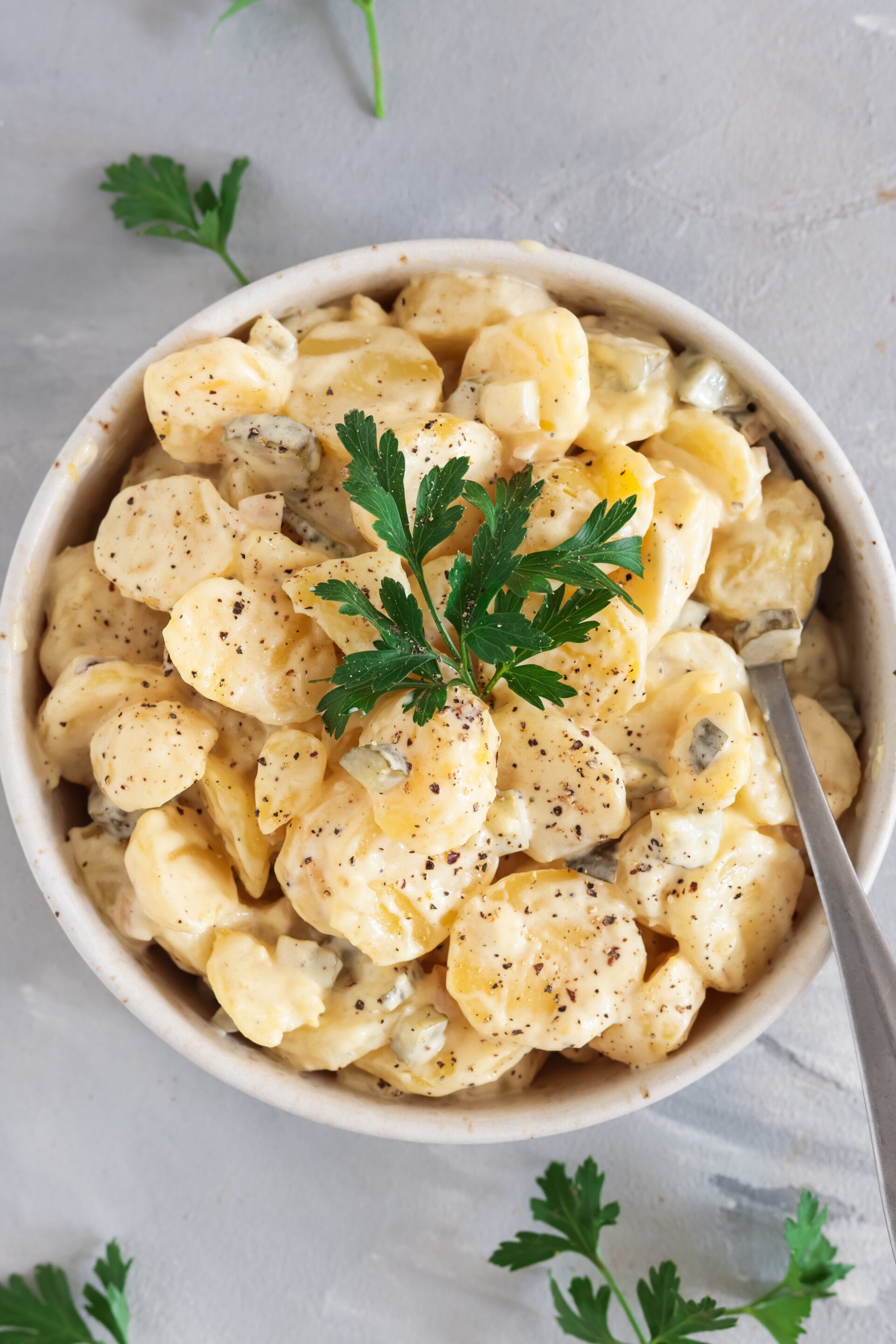 Veganer Kartoffelsalat mit Brühe und Mayo in heller Schale, garniert mit frischer Petersilie und Pfeffer