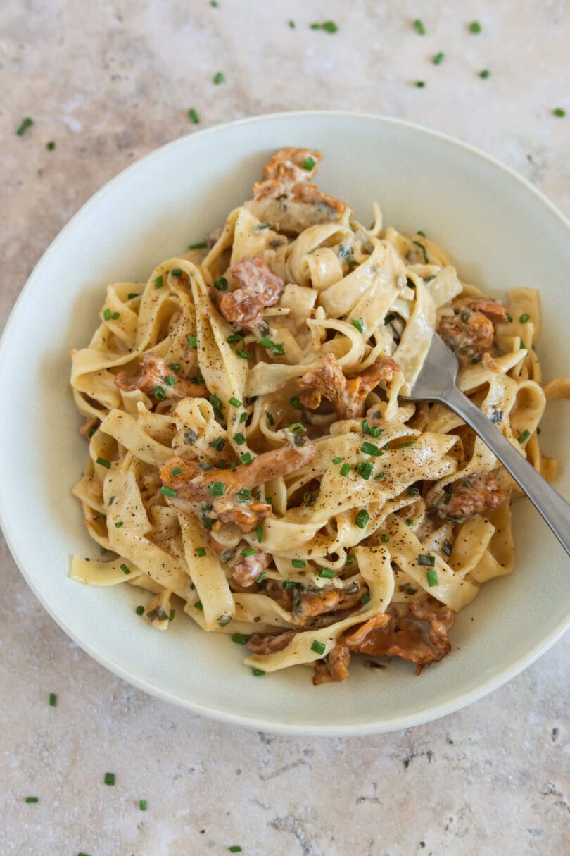 Cremige Pfifferling Pasta mit Bandnudeln in einer hellen Schale, garniert mit Schnittlauch und frisch gemahlenem Pfeffer.