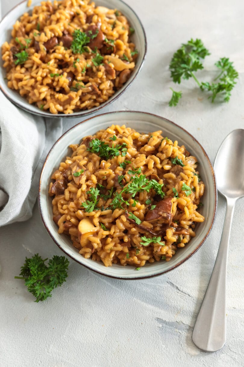 Veganes Steinpilzrisotto mit Pilzstücken und frischer Petersilie in einer Keramikschale.