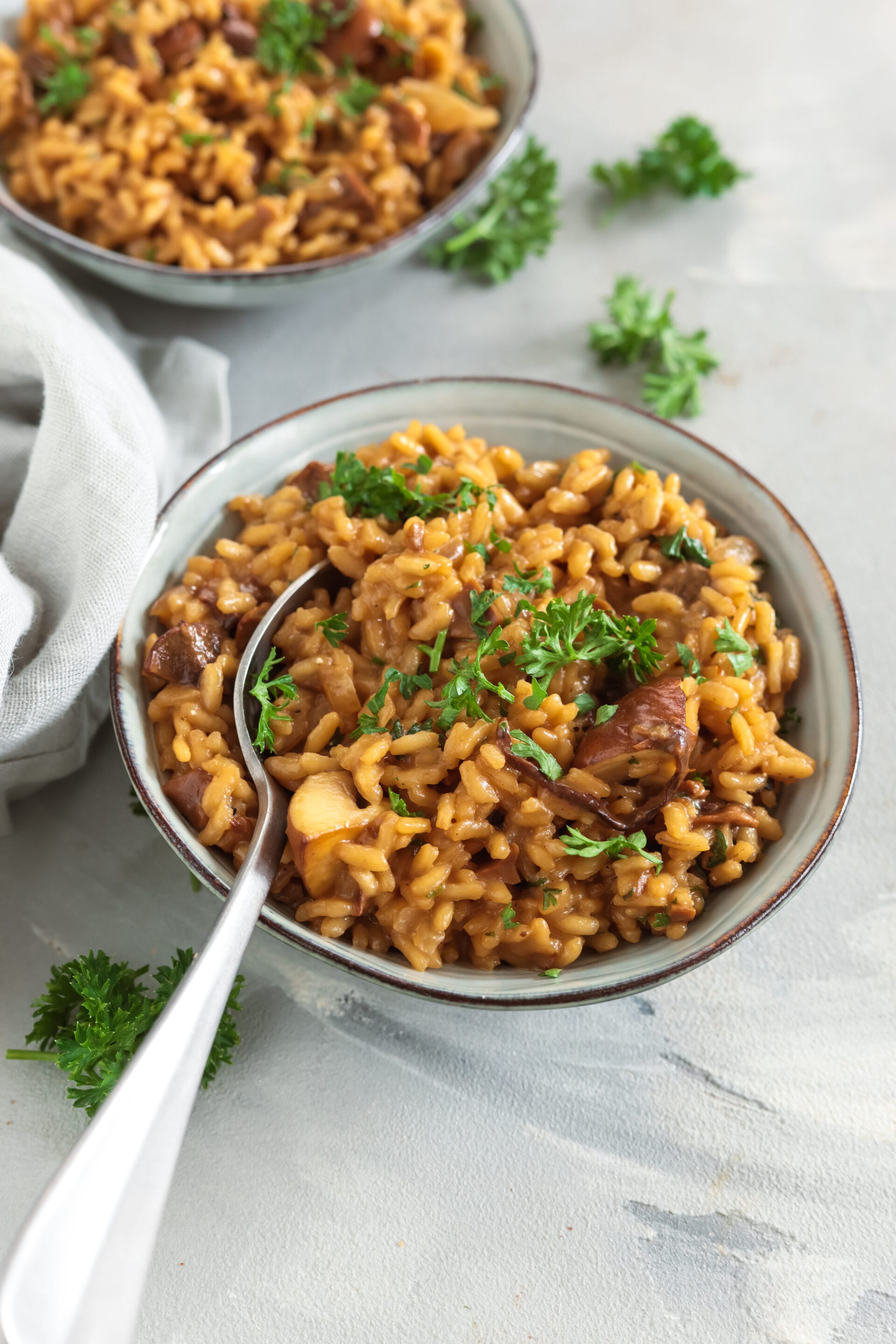 Nahaufnahme von cremigem Steinpilzrisotto mit Löffel, bestreut mit gehackter Petersilie.